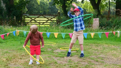 Two children play with hula hoops in a grassy field in summer